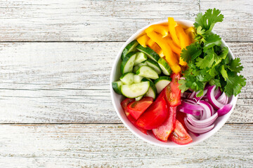 Plate of rainbow salad with different vegetables and herbs in white bowl on white wooden background