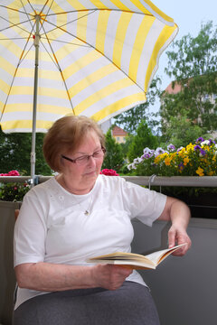 Frau Seniorin sitzt entspannt auf Balkon und liest Buch