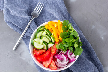 Plate of rainbow salad with different vegetables and herbs in white bowl on grey stone background