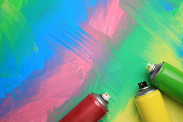 Cans of different spray paints on color background, flat lay with space for text. Graffiti supplies