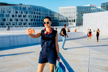 Loving female traveler making selfie with exterior view of the New Opera House, Operahuset in ...