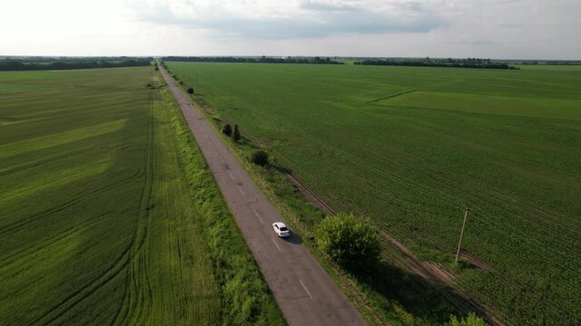 Drone footage of Volkswagen white car driving on the road past green fields