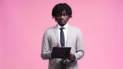 african american man in suit writing on clipboard isolated on pink - Powered by Adobe