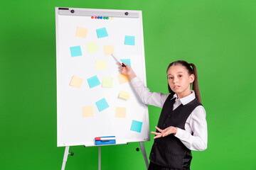 Fototapeta na wymiar Photo of pretty clueless school girl wear black white uniform pointing white board stickers isolated green color background