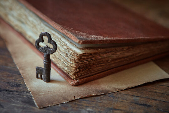 An ancient key of a beautiful shape stands next to a leather-bound parchment book.