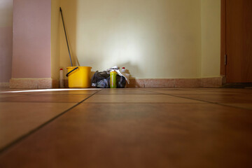 A mop and a bucket and cleaning products are standing in the corner on the tiled floor in the corridor