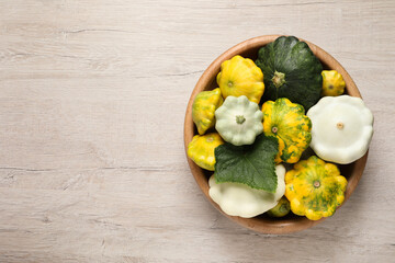 Fresh ripe pattypan squashes in bowl on light wooden table, top view. Space for text
