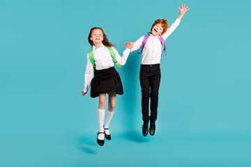 Photo of two funky dreamy kids jump go school wear rucksack white shirt uniform isolated blue color background