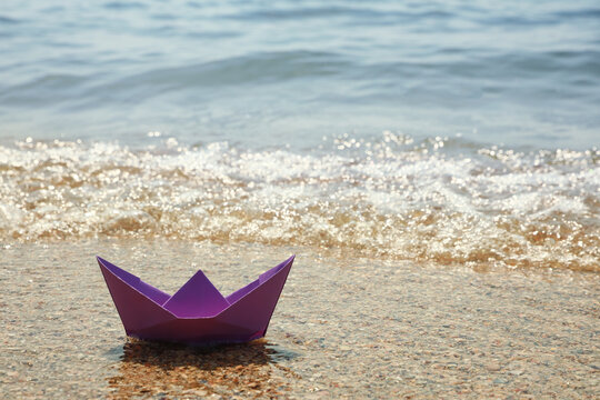 Purple paper boat near sea on sunny day, space for text