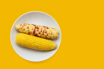 Boiled corn in white plate on yellow background.