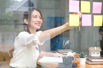 Smiling businessman putting sticky note reminder on the glass wall in office.