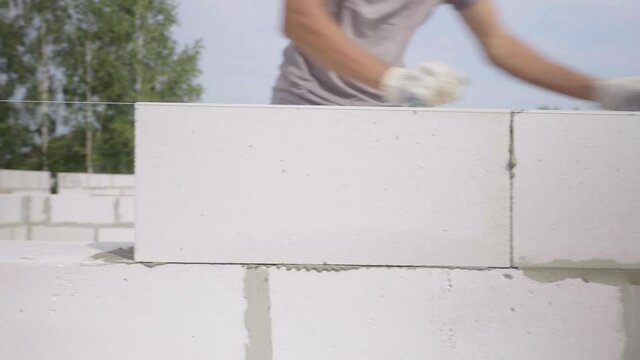 The hands of a bricklayer lay a wall of a white block close-up. A bricklayer Installs concrete blocks on a sunny day in summer. Contribution to the future and investment. business. Slow-motion action.