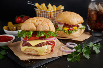 Two mouth-watering, Homemade hamburger with fresh vegetables and cheese lettuce and mayonnaise served, French fries on pieces of brown paper on black stone table . concept of fast food and junk food