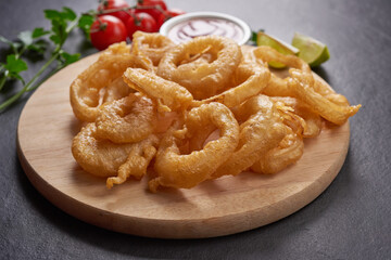 Homemade baked onion rings fries with mayonnaise, Tomato sauce and rosemary on wooden board. fast food products : onion rings on cutting board, on black stone background, unhealthy food.