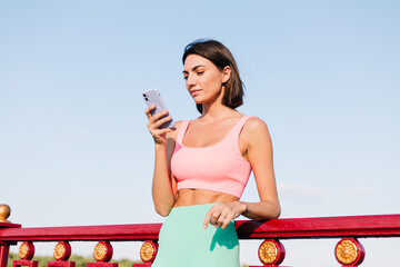 Sporty woman in fitting sport wear at sunset at modern bridge with river view happy positive smile...