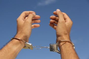 Man in handcuffs against blue sky outdoors, closeup