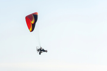 Side view of a paramotor vehicle flying in the sky from left to right of the image over a clear sky