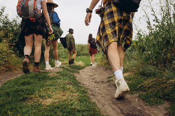 Group of friends, young men and women walking, strolling together outskirts of city, in summer forest, meadow. Active lifestyle, friendship, care, ecology concept