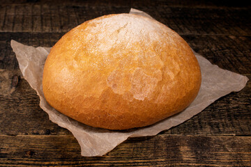 Round rye bread lying on a wooden table.Bread lying on the paper next to an old knife.