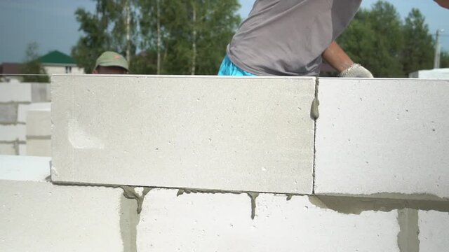 The hands of a bricklayer lay a wall of a white block close-up. A bricklayer Installs concrete blocks on a sunny day in summer. Contribution to the future and investment. business. Slow-motion action.