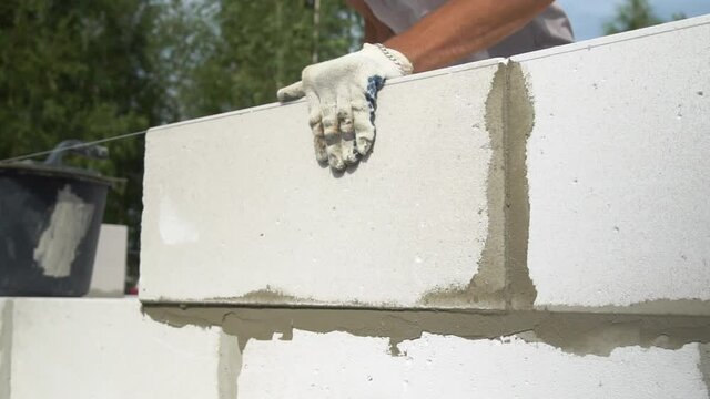 The hands of a bricklayer lay a wall of a white block close-up. A bricklayer Installs concrete blocks on a sunny day in summer. Contribution to the future and investment. business. Slow-motion action.