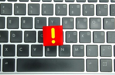a red cube with a yellow exclamation mark and a laptop background. The concept of exclamation marks.