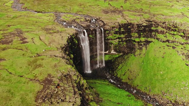 Aerial view of stunning waterfall in Faroe Islands. Aerial view of Fossa waterfall. Cloudy weather,establishing shot, no people. Majestic waterfall in wild rocky hillside. High quality footage.