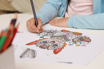 Fototapeta na wymiar Little girl coloring antistress page at table, closeup