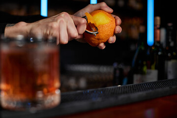 bartender makes a cocktail in a glass with orange peel