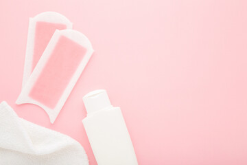 Wax strips, white cream bottle and towel on light pink table background. Pastel color. Closeup. Female products for smooth body skin. Empty place for text. Top down view.