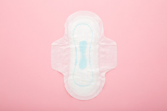 New opened white sanitary towel on light pink table background. Pastel color. Closeup. Female hygiene. Top down view.