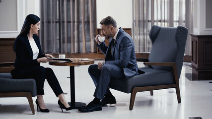 Businessman drinking coffee during business meeting with woman in restaurant lobby