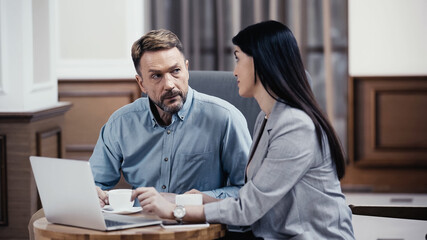 Business partners talking over coffee near laptop in lobby of restaurant