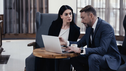 Businesswoman looking at man using laptop in restaurant lobby