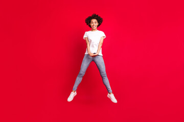 Fototapeta na wymiar Full length body size photo smiling curly woman jumping up happy isolated vivid red color background