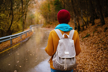 beautiful female hipster in a red hat, yellow sweater and blue scarf walks in the autumn nature....
