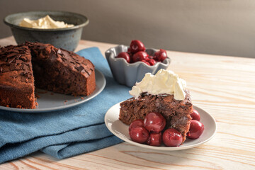 Rustic chocolate cake with morello cherries and whipped cream on a blue napkin and a wooden table, copy space, selected focus