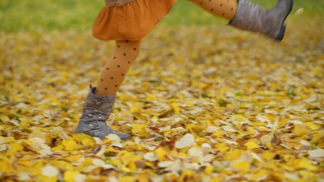 Hello september. Closeup on girl outside in the city park in autumn kicking autumn leaves.