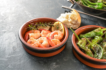 Spanish tapas in traditional bowls, fried pimientos or padron peppers and shrimps with lemon and...