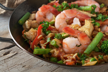 Rice dish with seafood, chicken and vegetables in a paella pan on a rustic wooden table, close up, selected focus