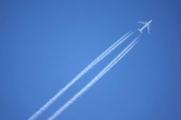 Large four engine passenger supersonic airplane flying from left to right high in blue cloudless sky leaving long white tracks - obrazy, fototapety, plakaty