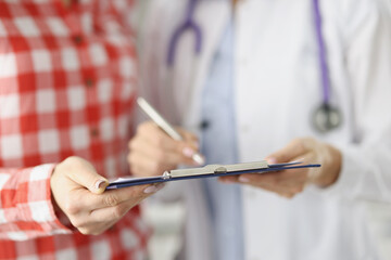 Doctor showing patient clipboard with documents in clinic closeup