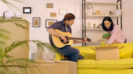 man playing acoustic guitar while woman unpacking books in new home