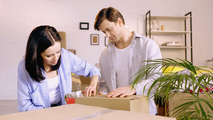 young couple using scotch tape while packing box