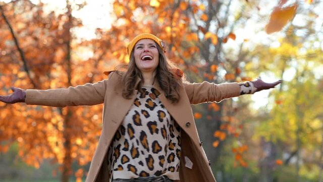 Hello november. smiling modern woman in beige coat and orange hat rejoicing outside in the city park in autumn. This video was made with PRORes 422 codec.