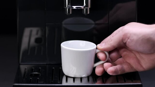 Close-up of a man's hand putting an empty espresso cup into an automatic coffee machine