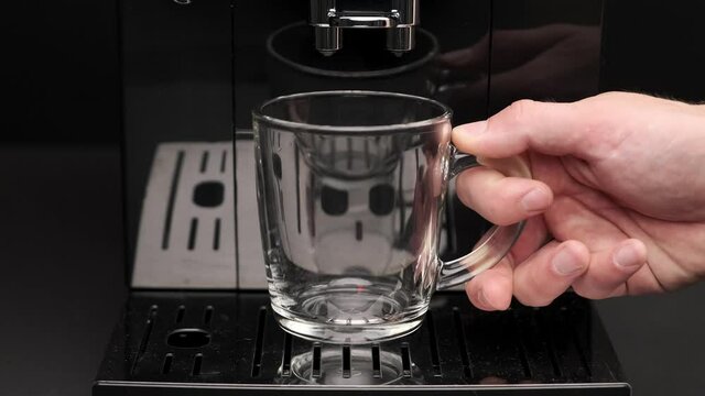A man's hand puts an empty transparent coffee cup in an automatic coffee machine in a close-up