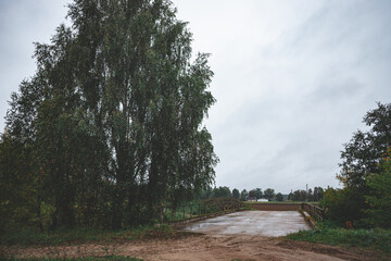 Fototapeta premium old concrete cement bridge over small river in Latvia countryside. Birch trees, cloudy grey sky. Dull september evening light