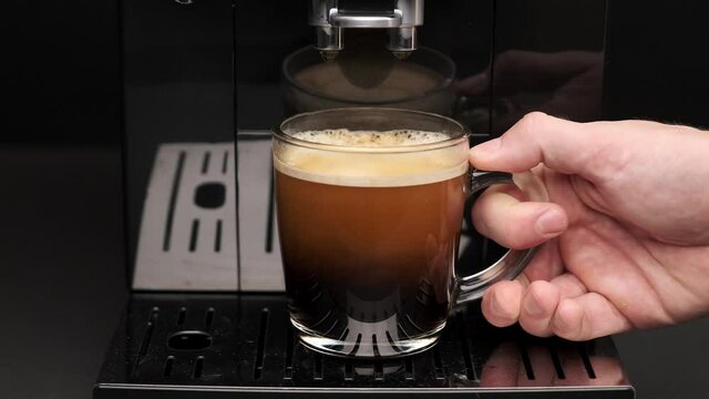 close-up of a man's hand taking freshly made coffee in a transparent glass