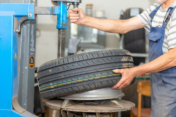 Mechanic changing tire in car service. Tire rotation machine.Car mechanic mounts tire on wheel in a...